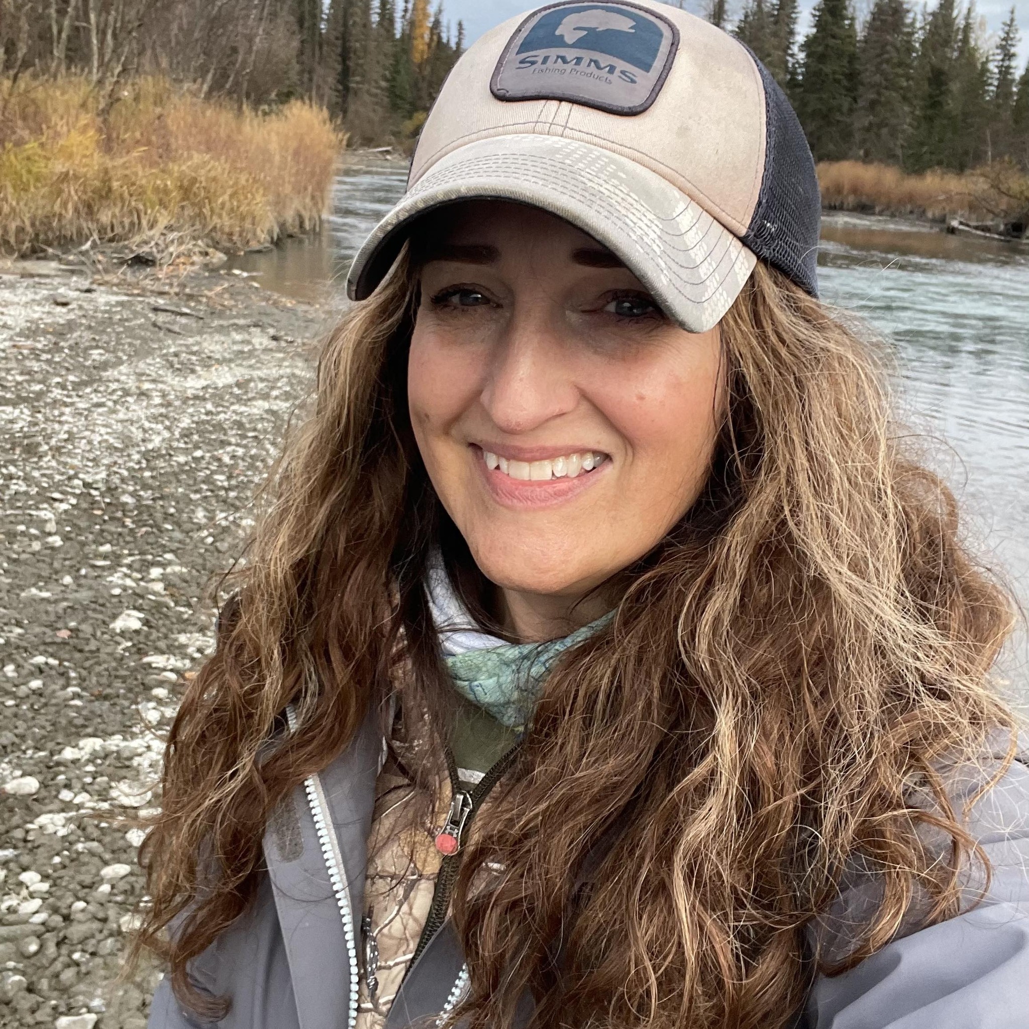 Image of KPBA Executive Director, Kirsten, in Simms hat with hair down and Kenai River in background.